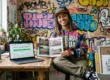 Mulher em estúdio mostrando livro aberto sobre graffiti brasileiro e notebook com campanha de crowdfunding financiada.